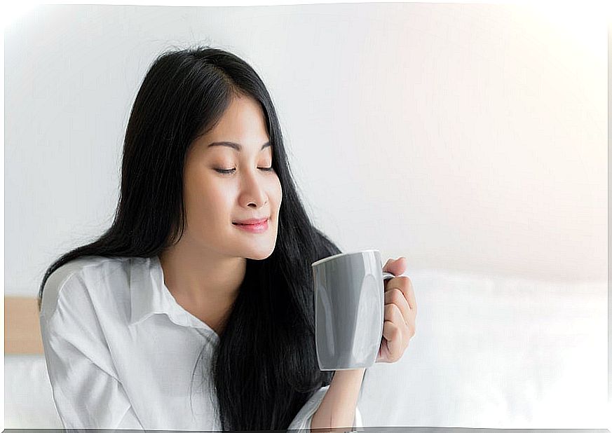 Woman with closed eyes with cup of tea in bed.