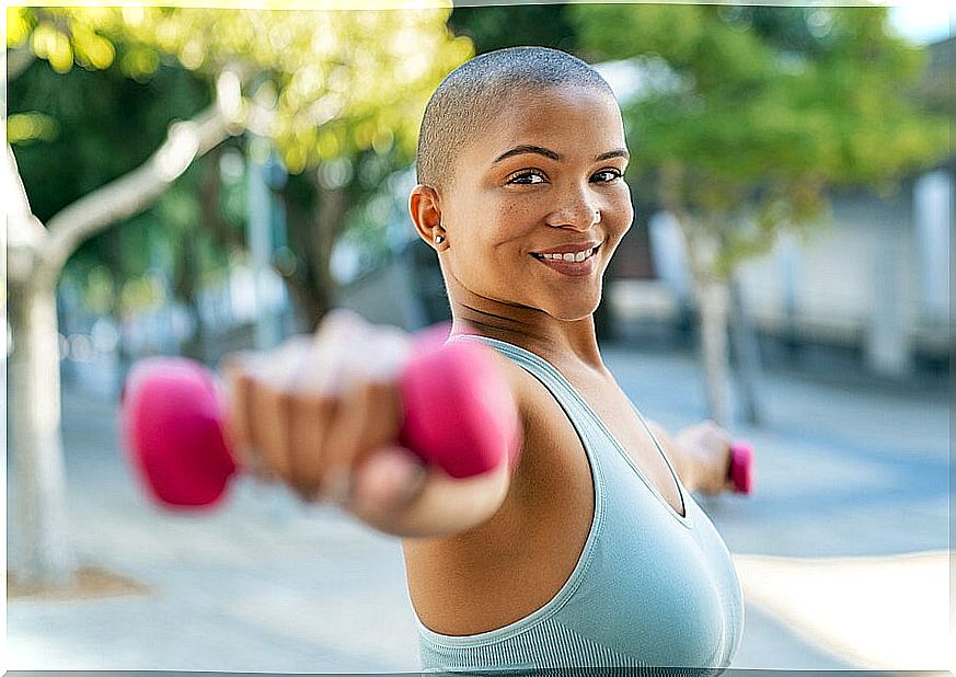 Woman doing exercises with the dumbbells to work the deltoids and build muscle mass in the arms.