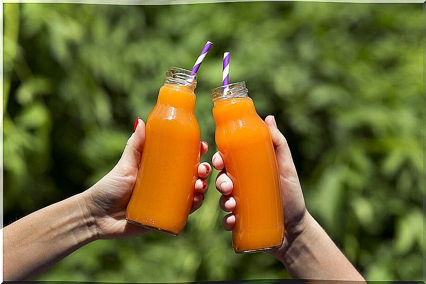 Hands holding bottles of carrot juice.